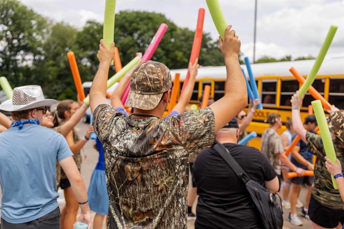 Staffers welcoming students off the buses with pool noodles on arrival day